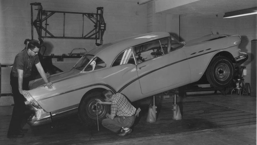 A black-and-white photo from the 1950s-1970s of two Kettering students inspecting a car tire in an automotive bay